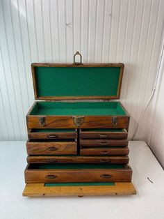 an old wooden chest with several drawers and green cloth on the bottom shelf, in front of a white wall