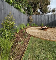 a garden with gravel and grass in front of a fenced in area that has a bowl on top of it