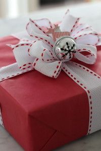 a red present box with white ribbon and a silver bell on the top is sitting on a table