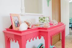 a pink table with pictures and seashells on it in front of a mirror