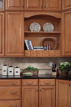 a kitchen with wooden cabinets and black granite counter tops in front of a basket filled with plants