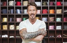 a man with his arms crossed in front of a shelf full of hats and ties