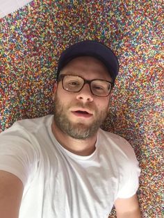 a man wearing glasses and a cap laying on the ground with sprinkles all over him