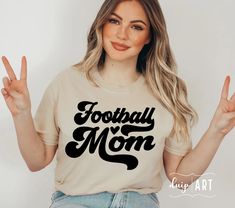 a woman wearing a t - shirt that says football mom with her hands in the air