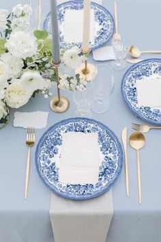 a blue and white table setting with place settings, silverware, napkins and flowers