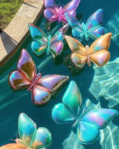 several colorful butterflies floating on top of the water in a pool with green grass and blue sky