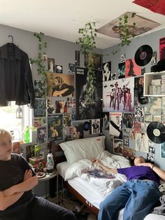 two people sitting on a bed in a room with posters and records all over the wall