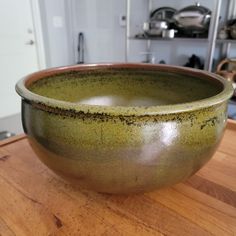 a large green bowl sitting on top of a wooden table next to a kitchen counter