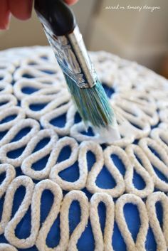 a close up of a person using a brush to paint the top of a blue cushion