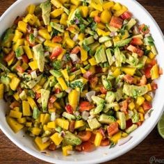 a white bowl filled with chopped vegetables and avocado on top of a wooden table