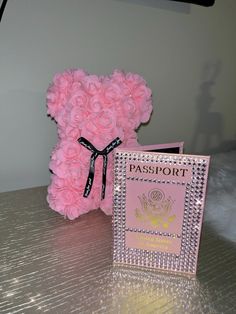 a pink teddy bear sitting next to a passport and card holder on top of a table