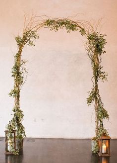 an arch made out of branches and candles is decorated with greenery for a wedding ceremony