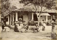 an old black and white photo of people sitting in front of a house with trees