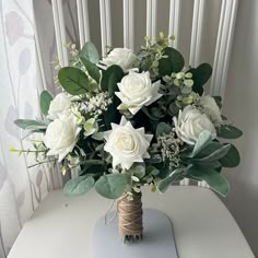 a bouquet of white roses and greenery on a table in front of a window