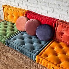 a multicolored couch sitting in front of a brick wall with pillows on it