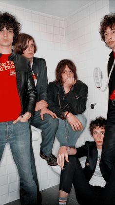 four young men sitting on a toilet in a bathroom with white tile walls and floor