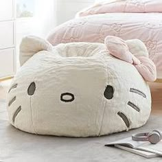 a cat shaped pillow sitting on top of a floor next to a bed and utensils