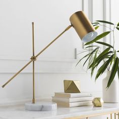 a white table with a gold lamp and some books on it next to a potted plant