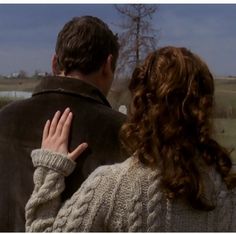 a man and woman standing next to each other in front of a field with trees