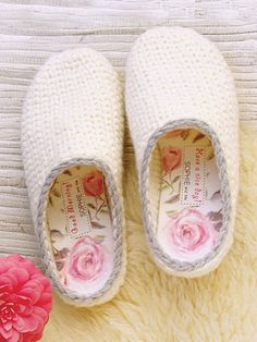 a pair of white slippers sitting on top of a rug next to a pink flower