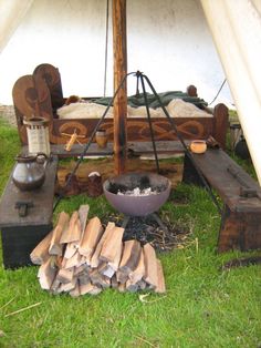 an outdoor fire pit surrounded by wood logs and other items on the grass in front of a tent