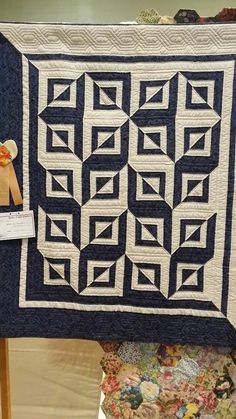 a blue and white quilt on display in a room with an orange ribbon hanging from the wall