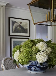 a vase filled with white flowers sitting on top of a dining room table next to a chandelier