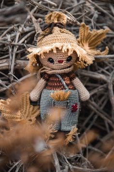 a knitted doll sitting on top of a pile of dry grass next to leaves