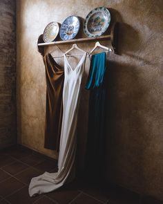 three dresses hanging on a rack in front of a wall with two plates and bowls