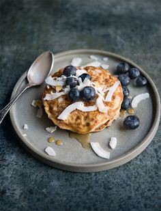 a plate topped with pancakes covered in blueberries and whip cream next to a spoon