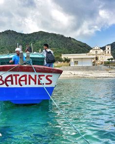 two men standing on the bow of a boat in clear blue water with mountains in the background