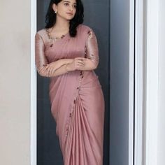 a woman in a pink sari standing by a door with her arms crossed and looking off to the side