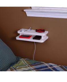 a bed with a pillow and a wall shelf on the side that has an electronic device plugged into it