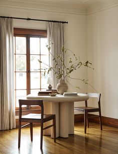 a table with two chairs and a vase filled with flowers on top of it next to a window