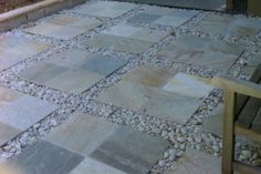 an outdoor patio with stones and gravel on the ground, next to a wooden bench