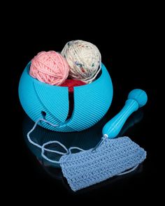 two balls of yarn and a crochet hook in a blue bowl on a black surface