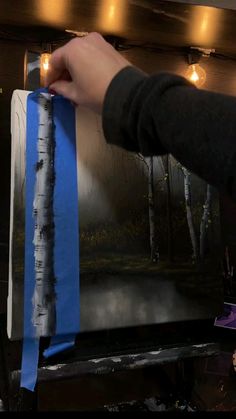 a person holding up a piece of blue tape to a painting on a easel