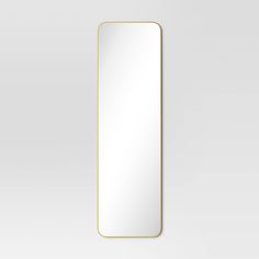 a rectangular mirror with a gold frame on a white wall, it is reflecting the light