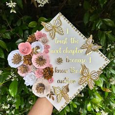 a hand holding a graduation cap with flowers on it that says trust the next chapter because know to believe