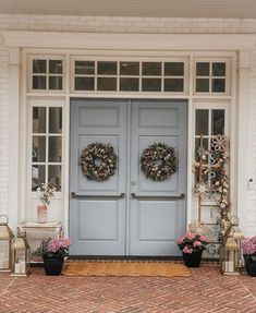 two blue front doors with wreaths on them and some flowers in black pots outside