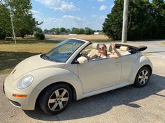 a man sitting in the driver's seat of a convertible car with his hands up