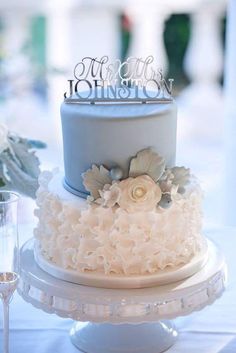 a wedding cake with flowers on it and the top tier is blue, white and silver