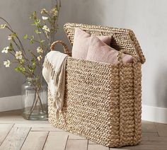 a basket sitting on the floor next to a vase with flowers in it and a throw pillow