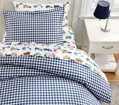 a blue and white checkered comforter set with trains on it, next to a night stand