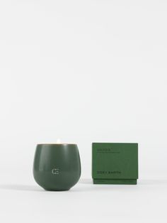 a green candle sitting next to a box on a white surface with a card in front of it