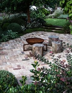 two wooden tables sitting on top of a brick patio next to bushes and trees in the background