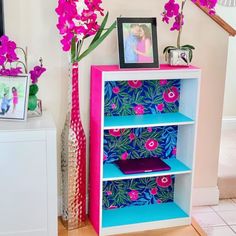 a pink and blue book shelf with flowers on top