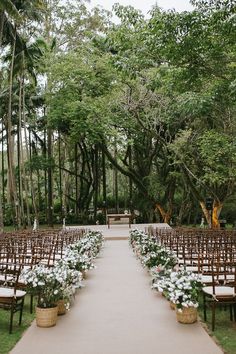 an outdoor ceremony setup with white flowers and greenery on the aisle, surrounded by tall trees