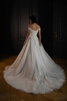 a woman in a white wedding dress standing on a wooden floor with her back to the camera