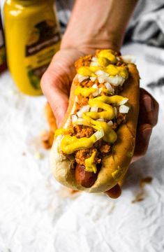 a person holding a hot dog with mustard and onions